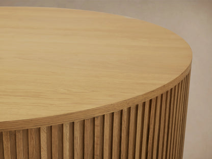 Finnley Round Wood Coffee Table in Honey finish, featuring a circular shape with vertical slats, placed on wooden flooring.