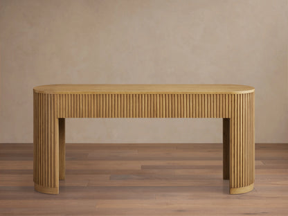 Finnley Wood Console Table with a Honey finish, features rounded edges and vertical grooves, set on a wooden floor against a beige wall.
