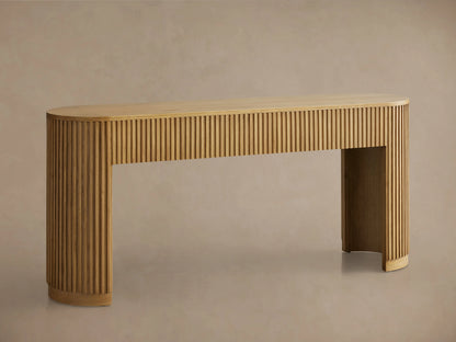 Finnley Wood Console Table with a Honey finish, features rounded edges and vertical grooves, set on a wooden floor against a beige wall.