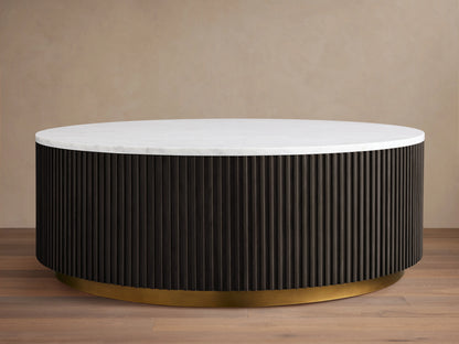 Finnley Round Coffee Table with a white marble top, dark ribbed cylindrical base, and brass-finished plinth on wooden floor.