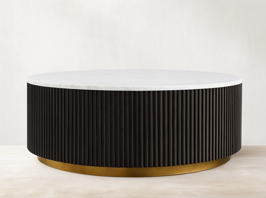 Finnley Round Coffee Table with a white marble top, dark ribbed cylindrical base, and brass-finished plinth on wooden floor.