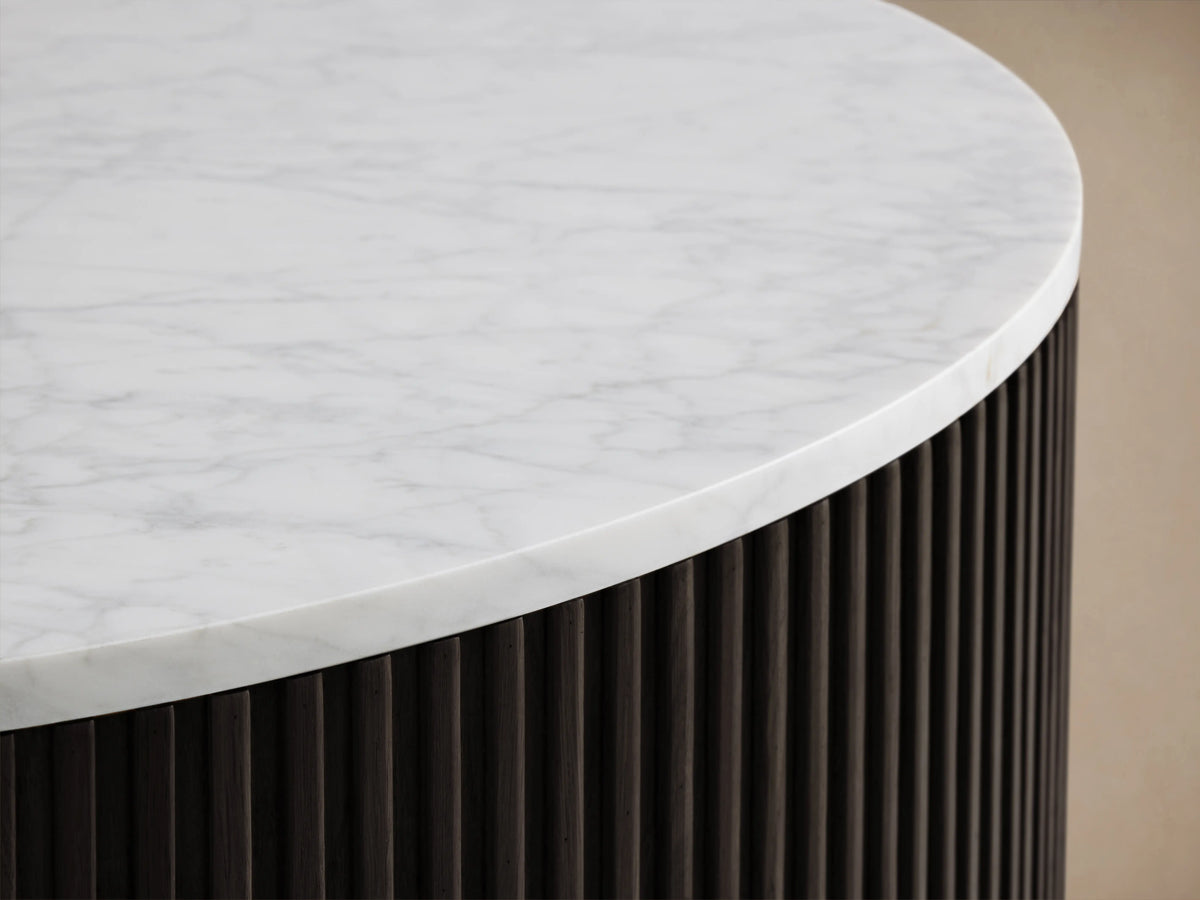 Finnley Round Coffee Table with a white marble top, dark ribbed cylindrical base, and brass-finished plinth on wooden floor.