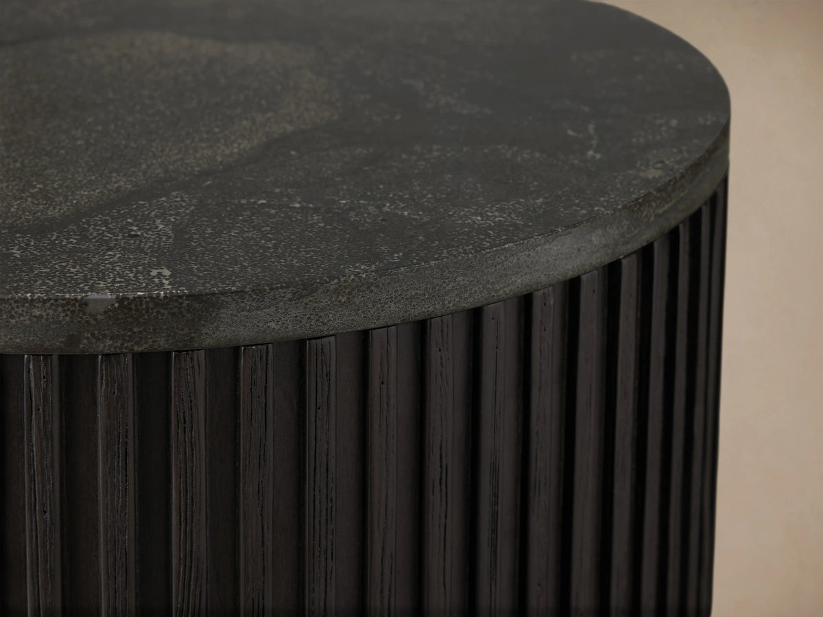 Finnley End Table with vertically ribbed dark wood surface, brass-finished base, standing on a wooden floor against a beige wall.