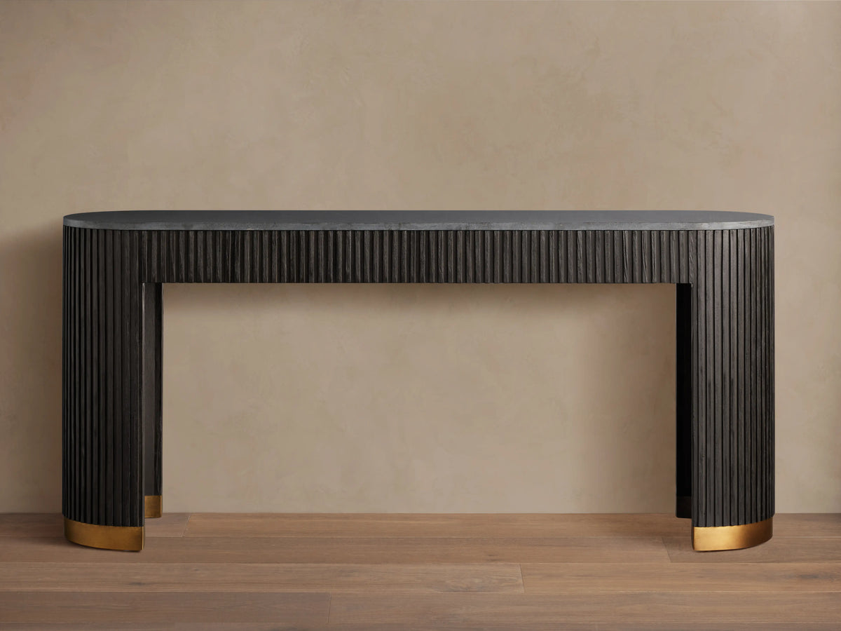 Finnley Console Table in dark wood with vertical ridges, brass-finished plinth bases, set on a wooden floor against a beige wall.