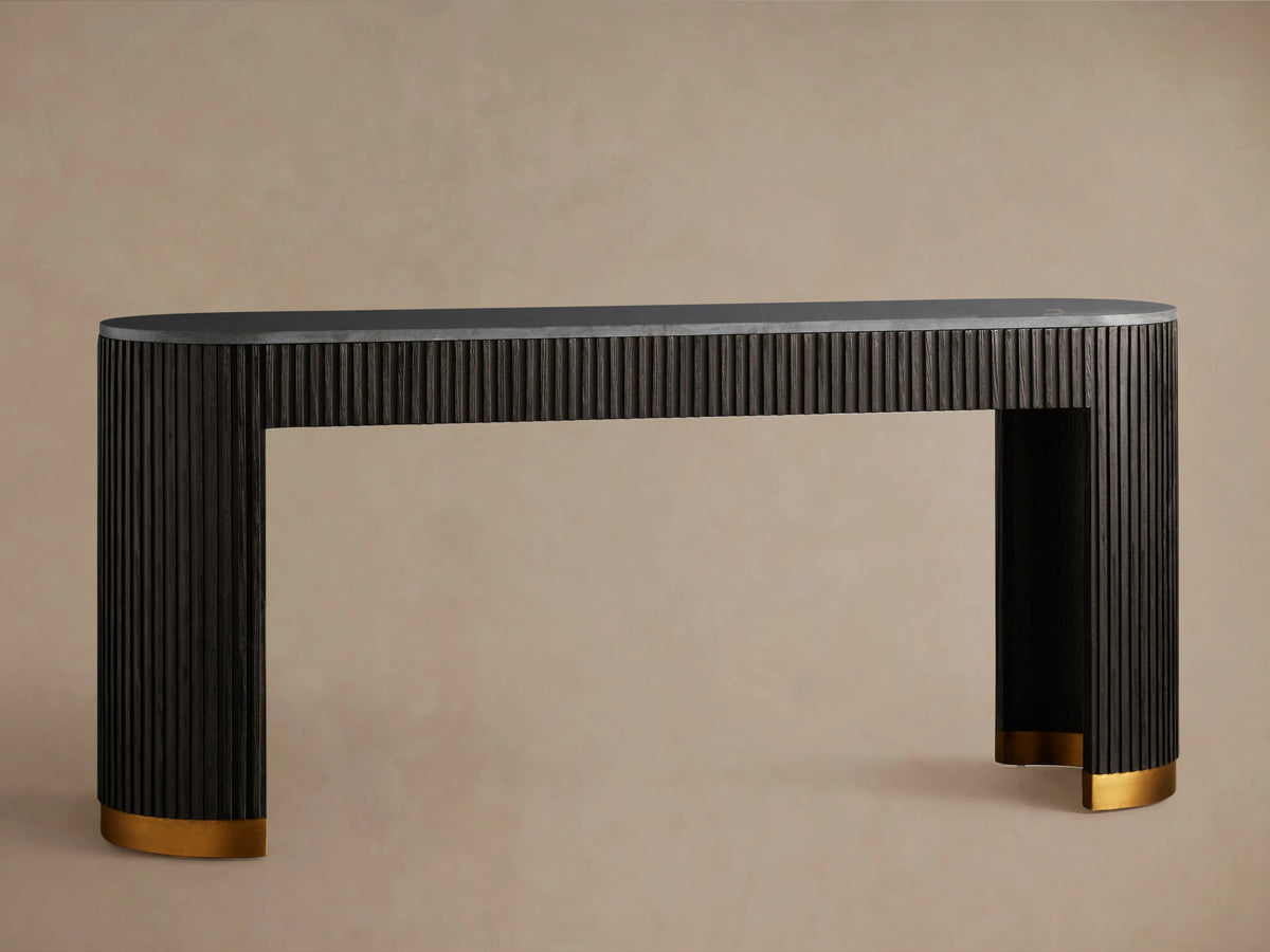 Finnley Console Table in dark wood with vertical ridges, brass-finished plinth bases, set on a wooden floor against a beige wall.