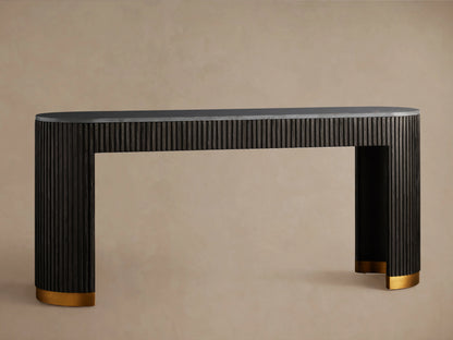 Finnley Console Table in dark wood with vertical ridges, brass-finished plinth bases, set on a wooden floor against a beige wall.