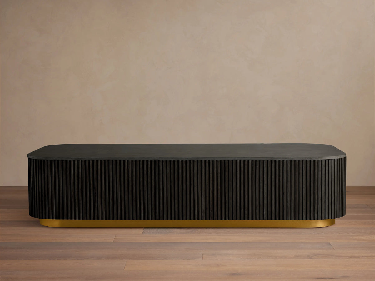 Finnley Coffee Table with a rectangular shape, ebony finish, ribbed sides, and a brass-finished base, on a wooden floor.