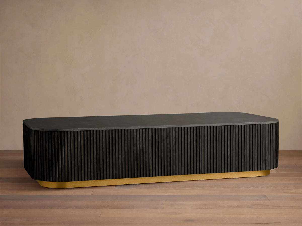 Finnley Coffee Table with a rectangular shape, ebony finish, ribbed sides, and a brass-finished base, on a wooden floor.