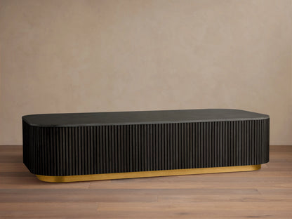 Finnley Coffee Table with a rectangular shape, ebony finish, ribbed sides, and a brass-finished base, on a wooden floor.