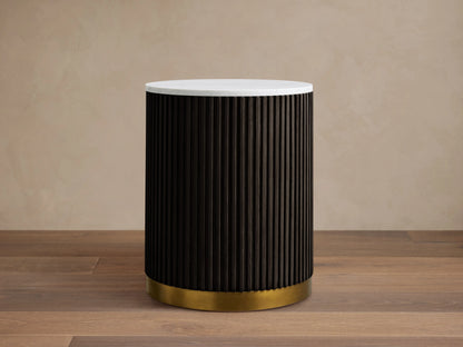 Finnley End Table with vertical dark ribbed sides, white round top, and brass-finished base on a wooden floor.