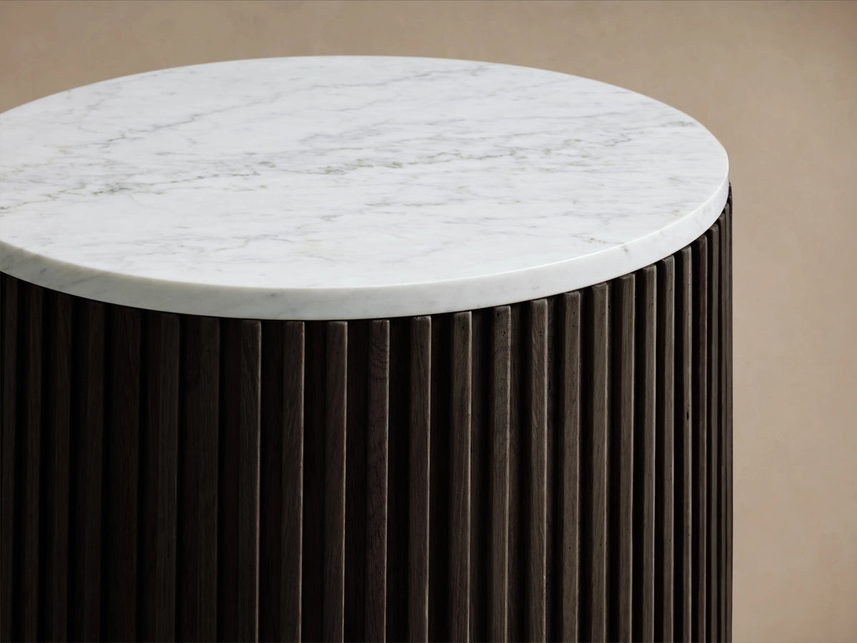 Finnley End Table with vertical dark ribbed sides, white round top, and brass-finished base on a wooden floor.