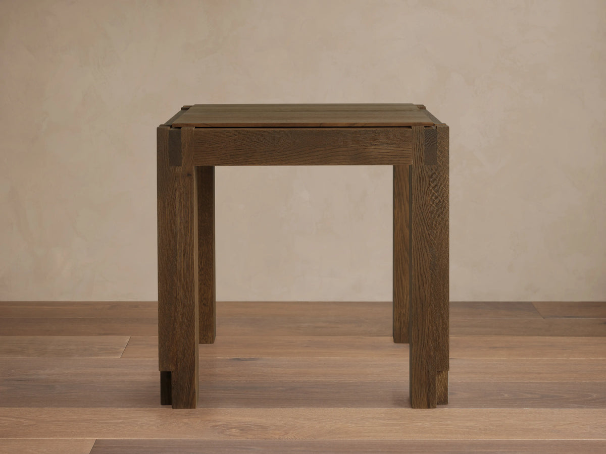 Harlan End Table made of solid oak wood with a square top, clean lines, and a brown stained finish. Placed on wooden floor.