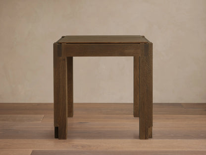 Harlan End Table made of solid oak wood with a square top, clean lines, and a brown stained finish. Placed on wooden floor.