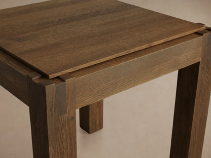 Harlan End Table made of solid oak wood with a square top, clean lines, and a brown stained finish. Placed on wooden floor.