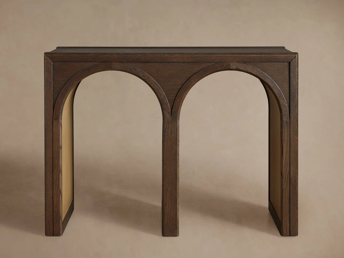 Hattie Console Table made of dark solid oak wood with two arches. A white ceramic bowl and a closed book are on top. Contrasting interiors.