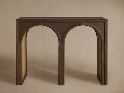 Hattie Console Table made of dark solid oak wood with two arches. A white ceramic bowl and a closed book are on top. Contrasting interiors.