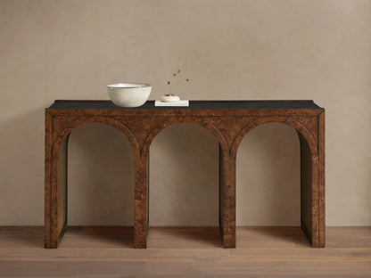 Hattie Burl Console Table: brown burl wood with three arches, dark top, neutral bowl & small decor items on top, against a beige wall.