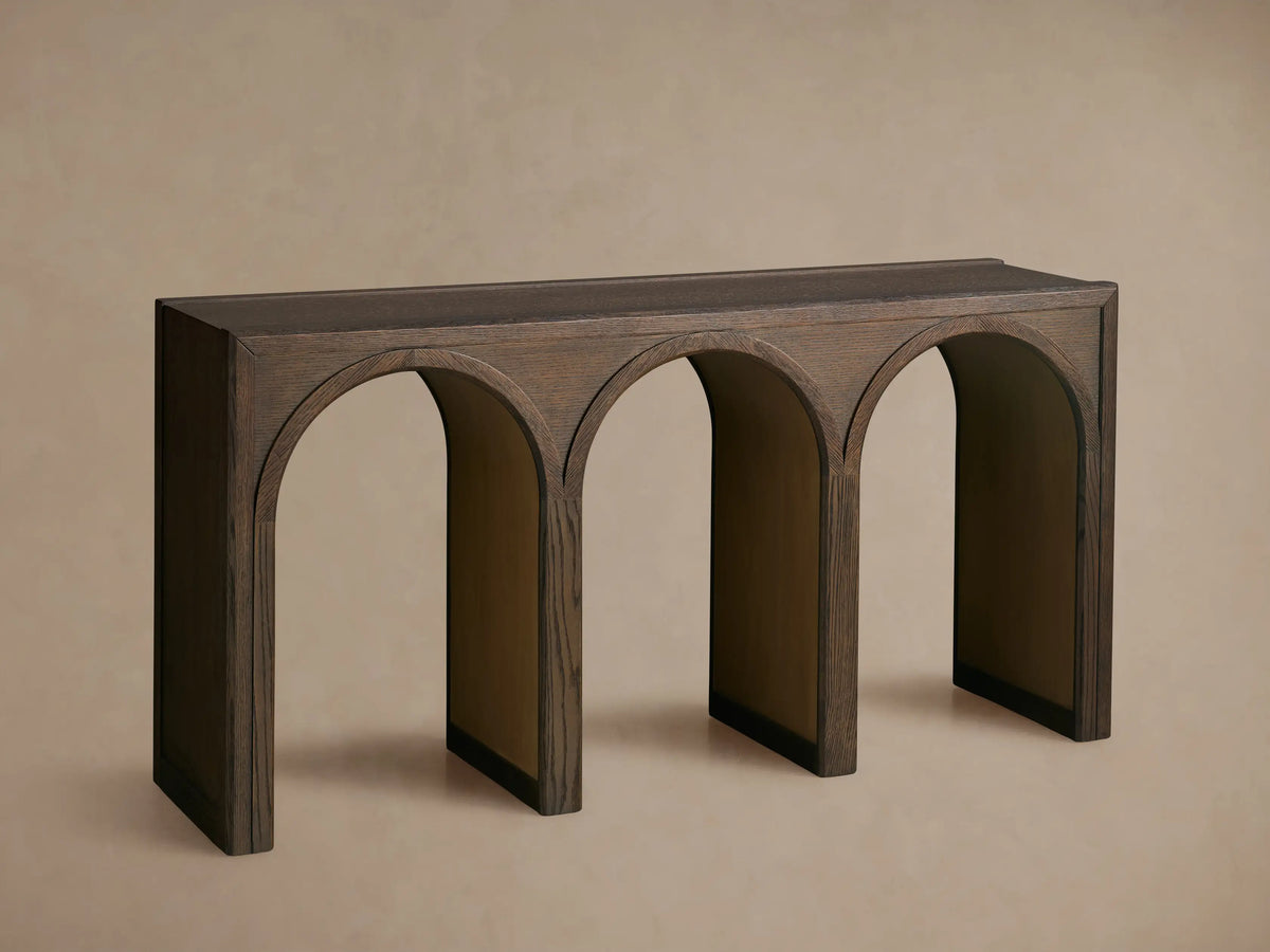 Dark brown Hattie Console Table with 3 arched supports, contrasting light tan interiors, against a beige wall and wood floor.