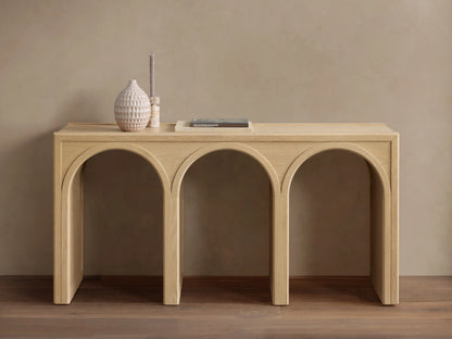 Oak Hattie Console Table with three arch-shaped supports, light wood finish, vase, book, and candle displayed on top.