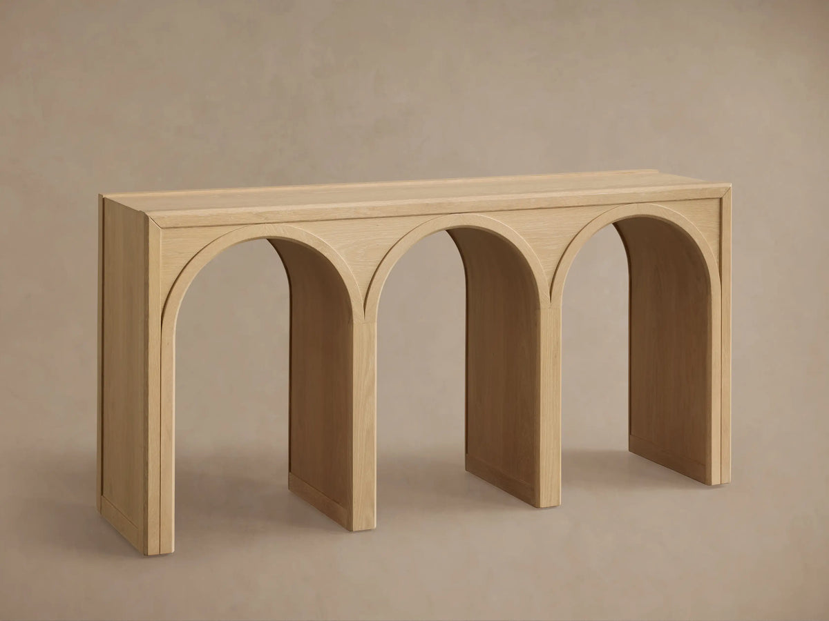 Oak Hattie Console Table with three arch-shaped supports, light wood finish, vase, book, and candle displayed on top.