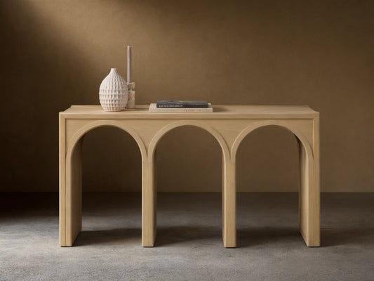 Oak Hattie Console Table with three arch-shaped supports, light wood finish, vase, book, and candle displayed on top.