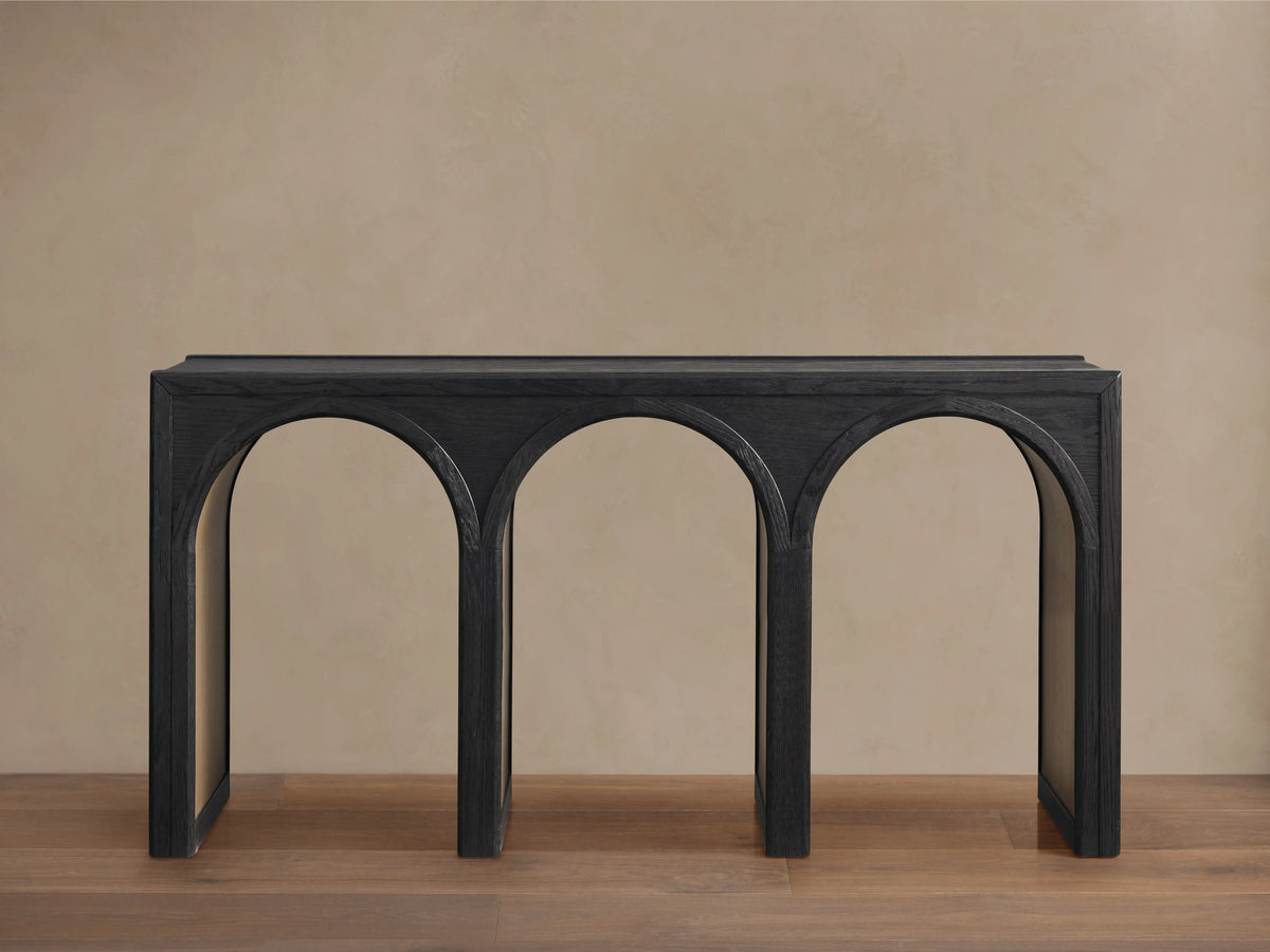 Hattie Console Table in dark oak, showcasing a rectangular top with three arch-shaped legs against a light brown wall and wood floor.