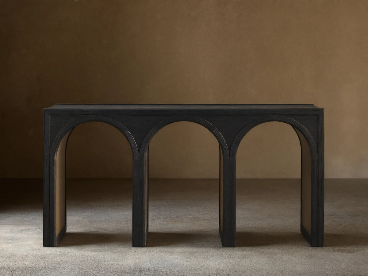 Hattie Console Table in dark oak, showcasing a rectangular top with three arch-shaped legs against a light brown wall and wood floor.