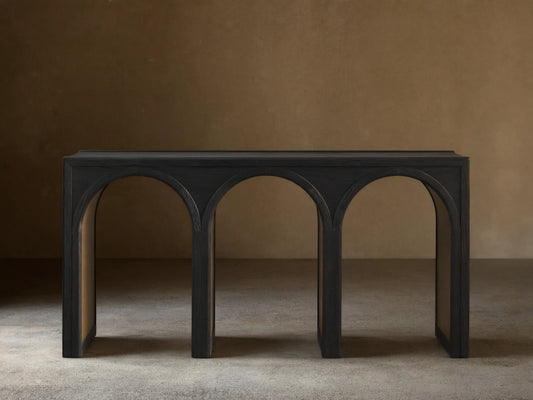 Hattie Console Table in dark oak, showcasing a rectangular top with three arch-shaped legs against a light brown wall and wood floor.
