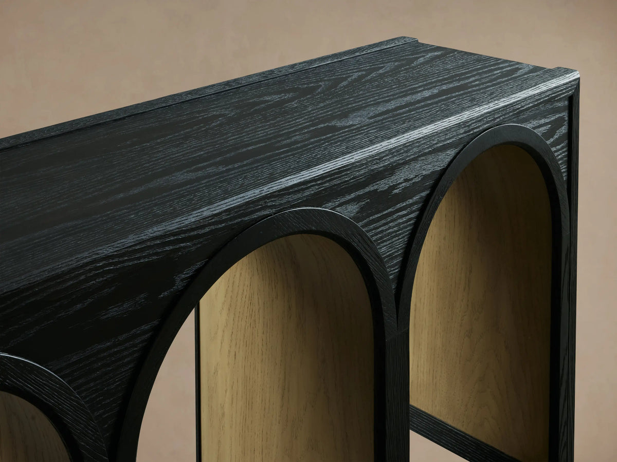 Hattie Console Table made of dark solid oak, featuring multiple arched legs with contrasting inner finishes on a wooden floor.