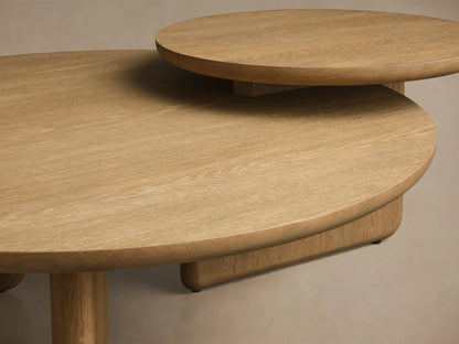 Front view of the light oak Nested Coffee Table Set, showing two round tables with thick bases, one partially tucked under the other.