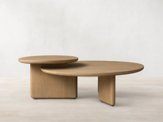 Front view of the light oak Nested Coffee Table Set, showing two round tables with thick bases, one partially tucked under the other.