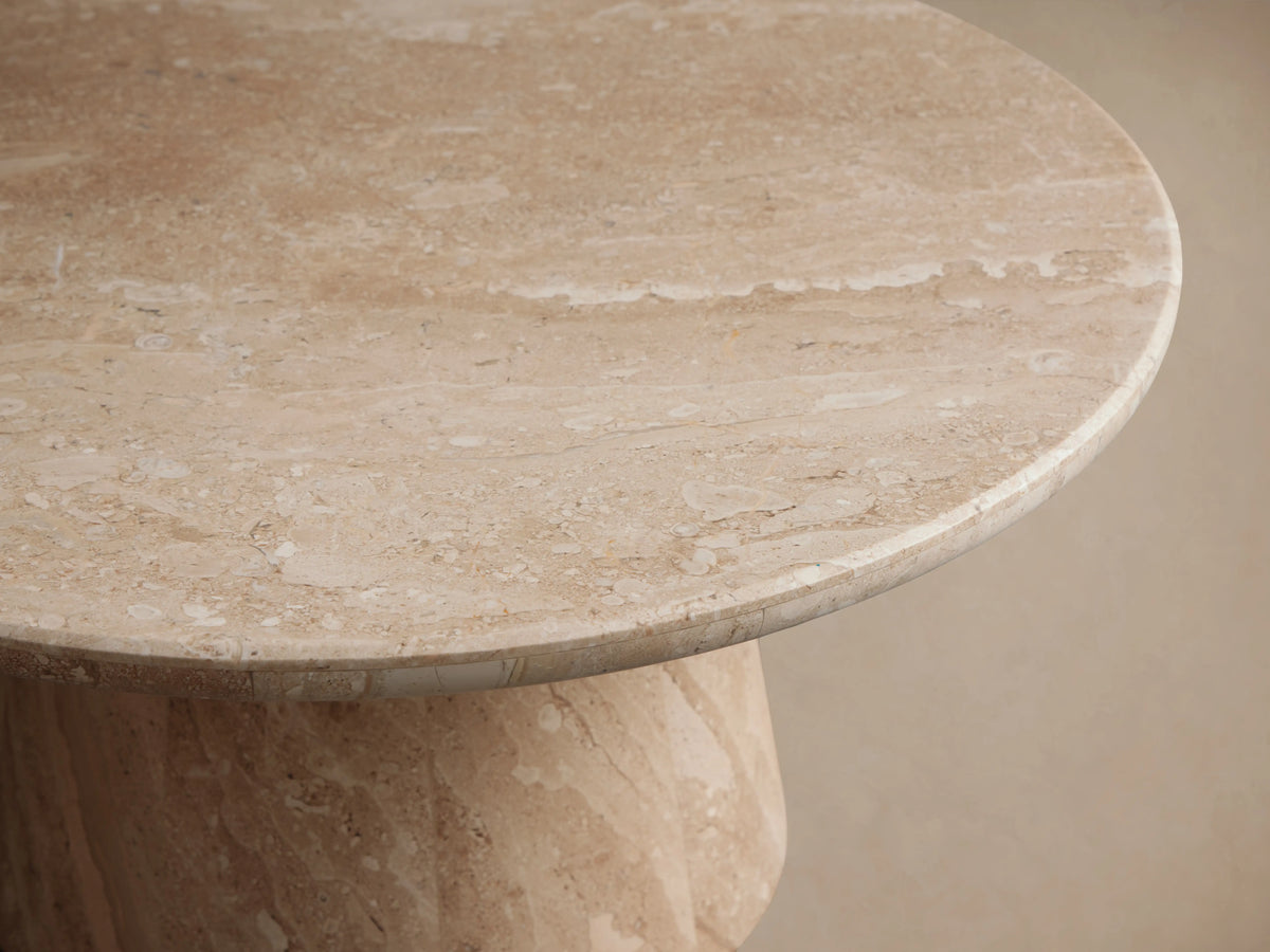 Hemmings Stone Nesting Coffee Table, round light beige stone with natural veining and a tapered base, on a wooden floor.