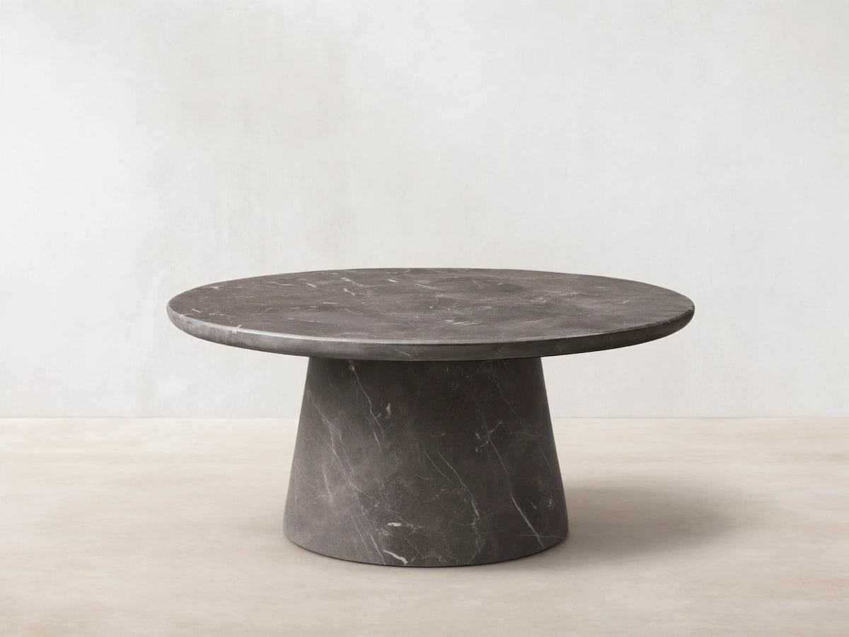 Front view of a dark gray round marble coffee table with prominent white veining, featuring a thick round top and a conical base.