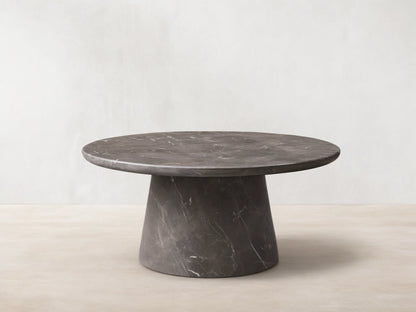 Front view of a dark gray round marble coffee table with prominent white veining, featuring a thick round top and a conical base.