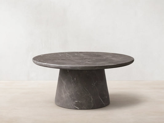 Front view of a dark gray round marble coffee table with prominent white veining, featuring a thick round top and a conical base.
