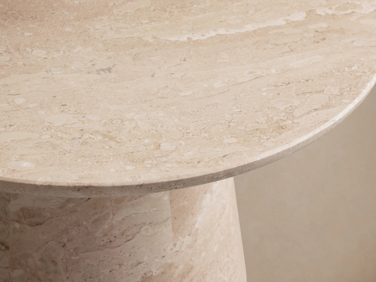 Round beige coralle marble table with a smooth top and a conical base, featuring subtle natural patterns, on a wooden floor.
