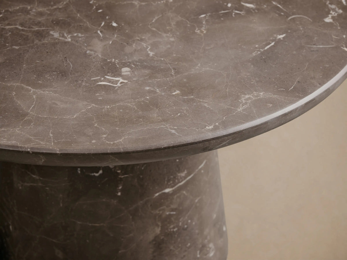 Close-up of a dark gray-brown marble table with white veining, showing the smooth round top and part of the base.