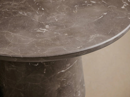 Close-up of a dark gray-brown marble table with white veining, showing the smooth round top and part of the base.