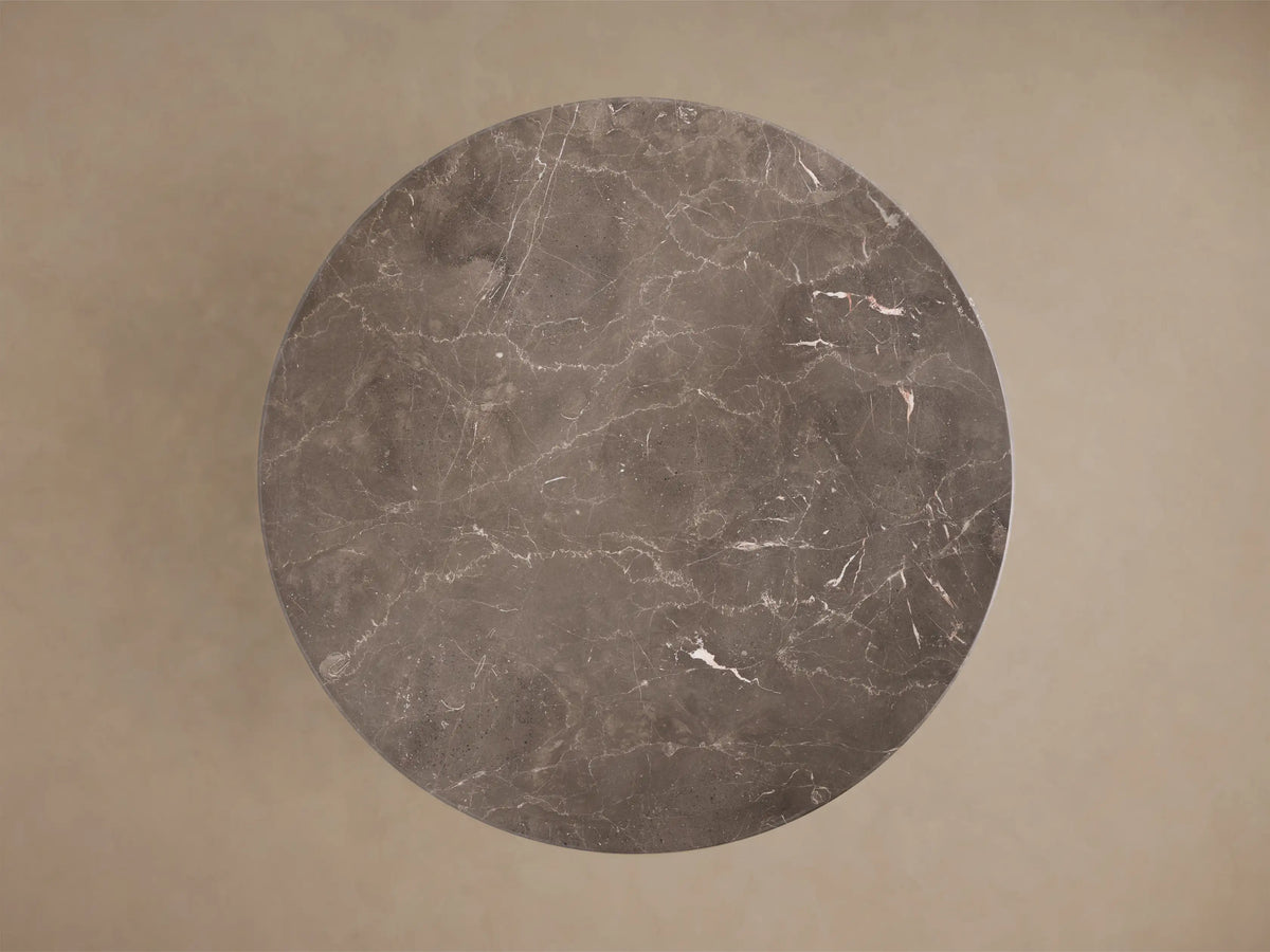 Front view of a round brownish-gray marble table with white veining, featuring a thick tapered pedestal base.