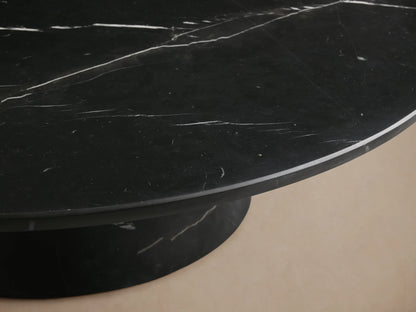 Hemmings Stone Coffee Table with a round black marble top and conical base, featuring prominent white veining, set on a wood floor.