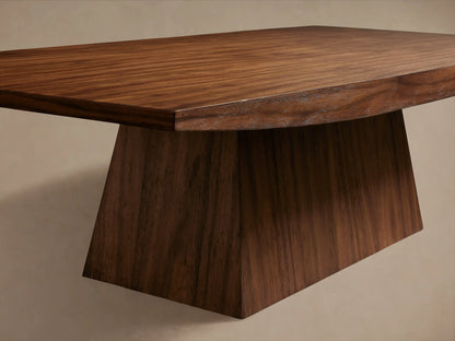 Ilaria Coffee Table with a wide, flat wooden top and unique angular base in rich brown finish, set on wooden floor.