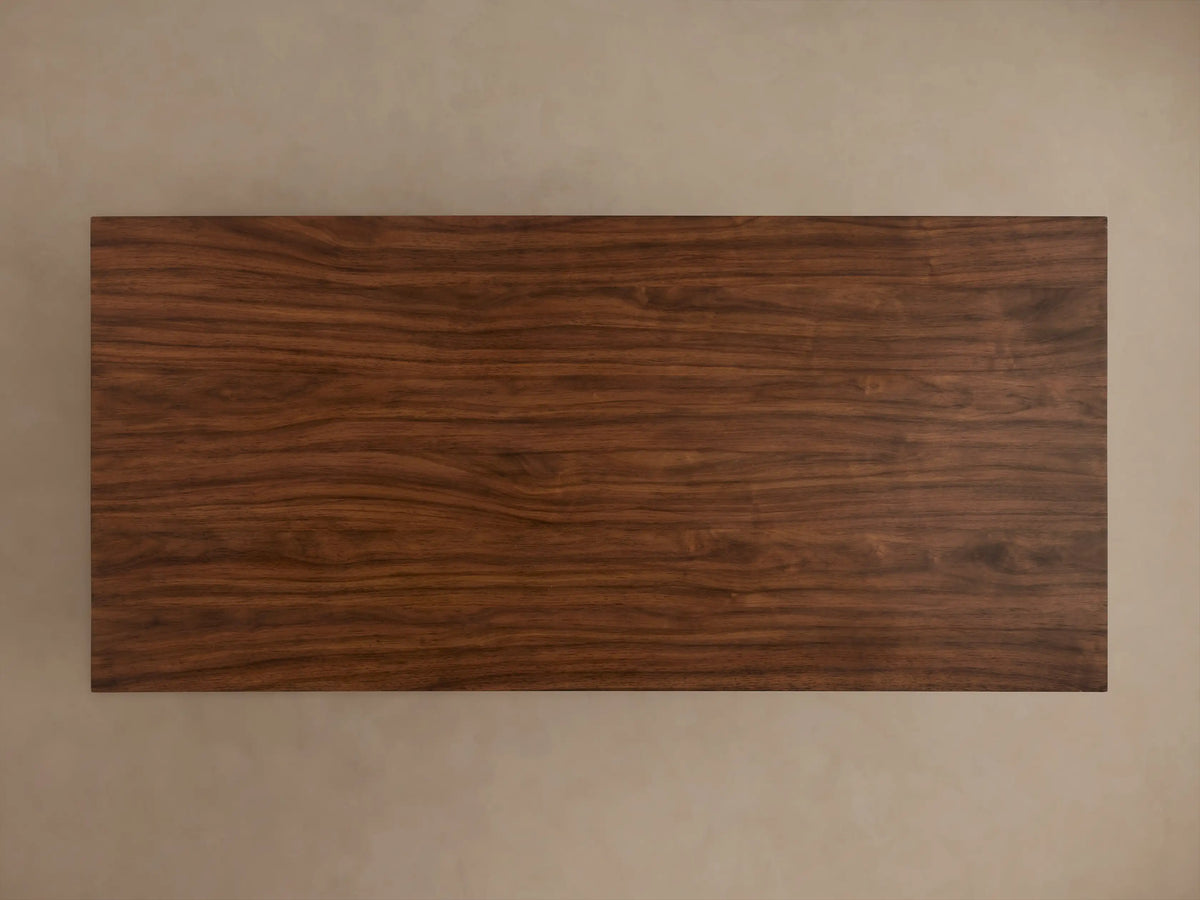 Ilaria Coffee Table with a sleek rectangular wooden top and a wide, trapezoidal base. The rich brown wood grain is prominently visible.