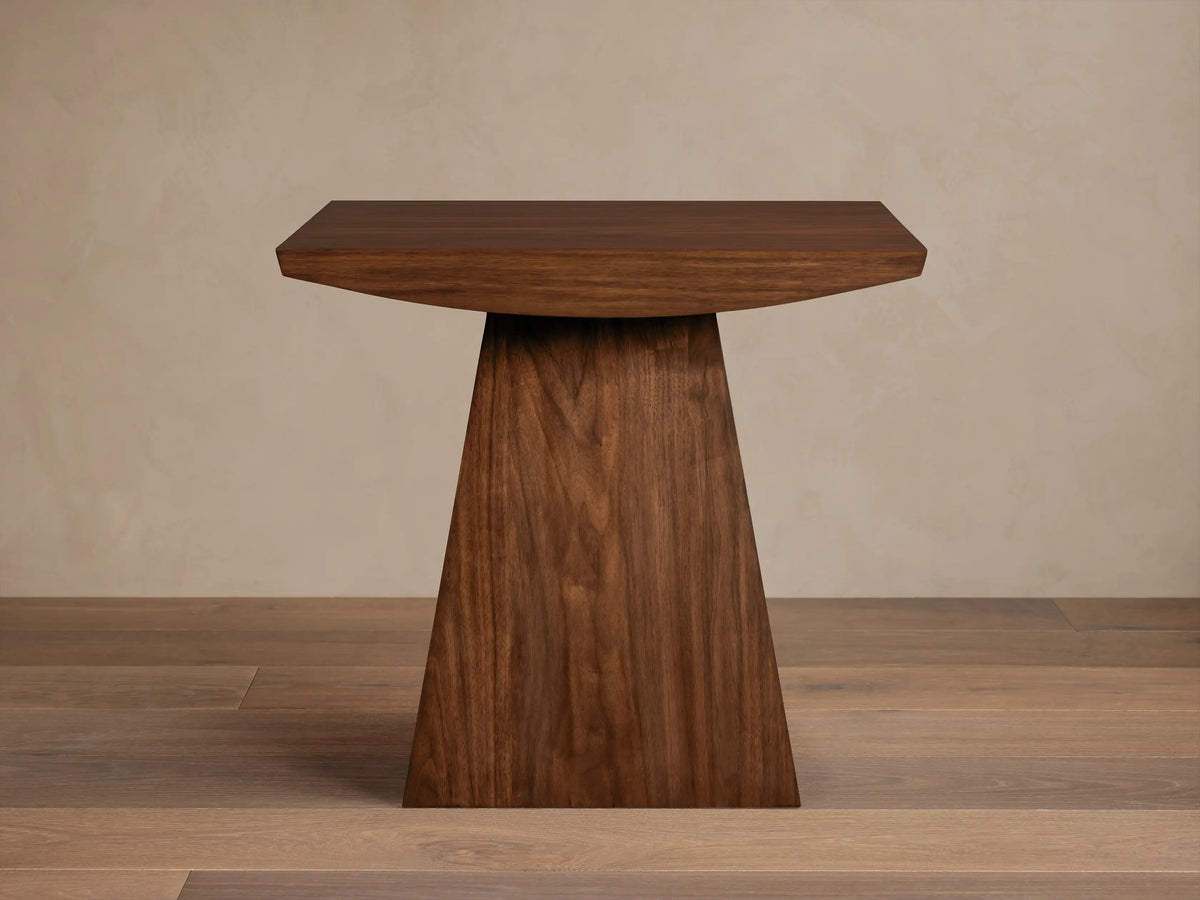 Ilaria End Table featuring a travertine top with smooth edges and a tapered wooden base on a wooden floor.