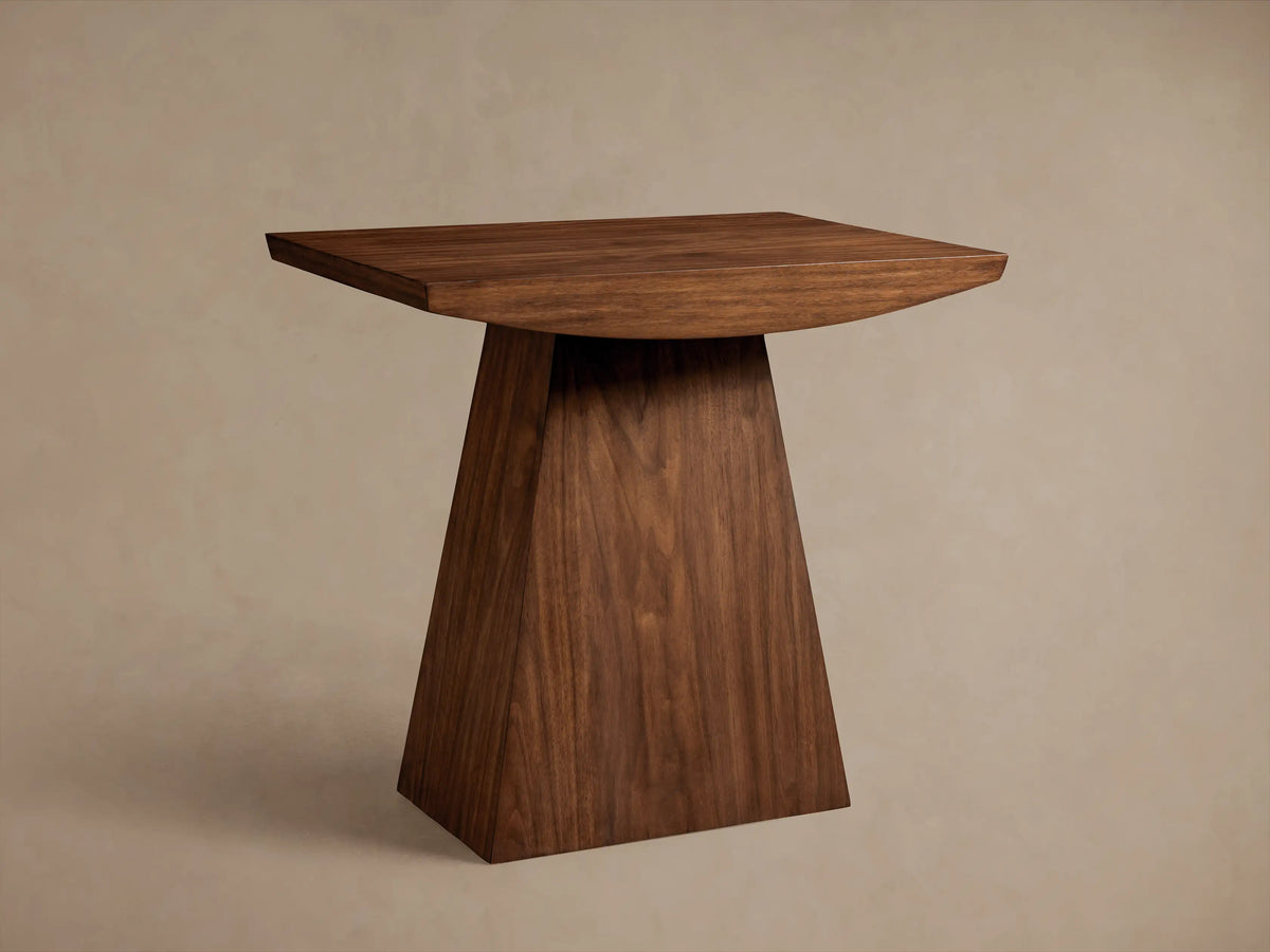 Ilaria End Table featuring a travertine top with smooth edges and a tapered wooden base on a wooden floor.