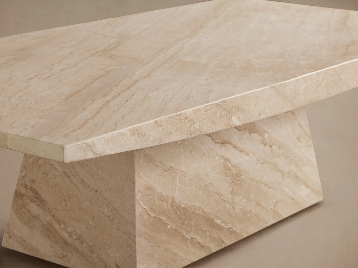 A beige marble coffee table with a geometric design, featuring a wide rectangular top and a trapezoidal base, on a wooden floor.