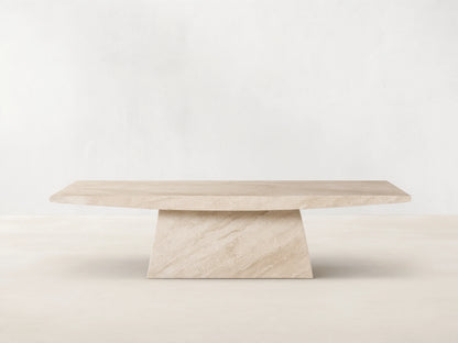 A beige marble table with a rectangular top and an angled, trapezoidal base. Positioned on a wooden floor against a plain wall.