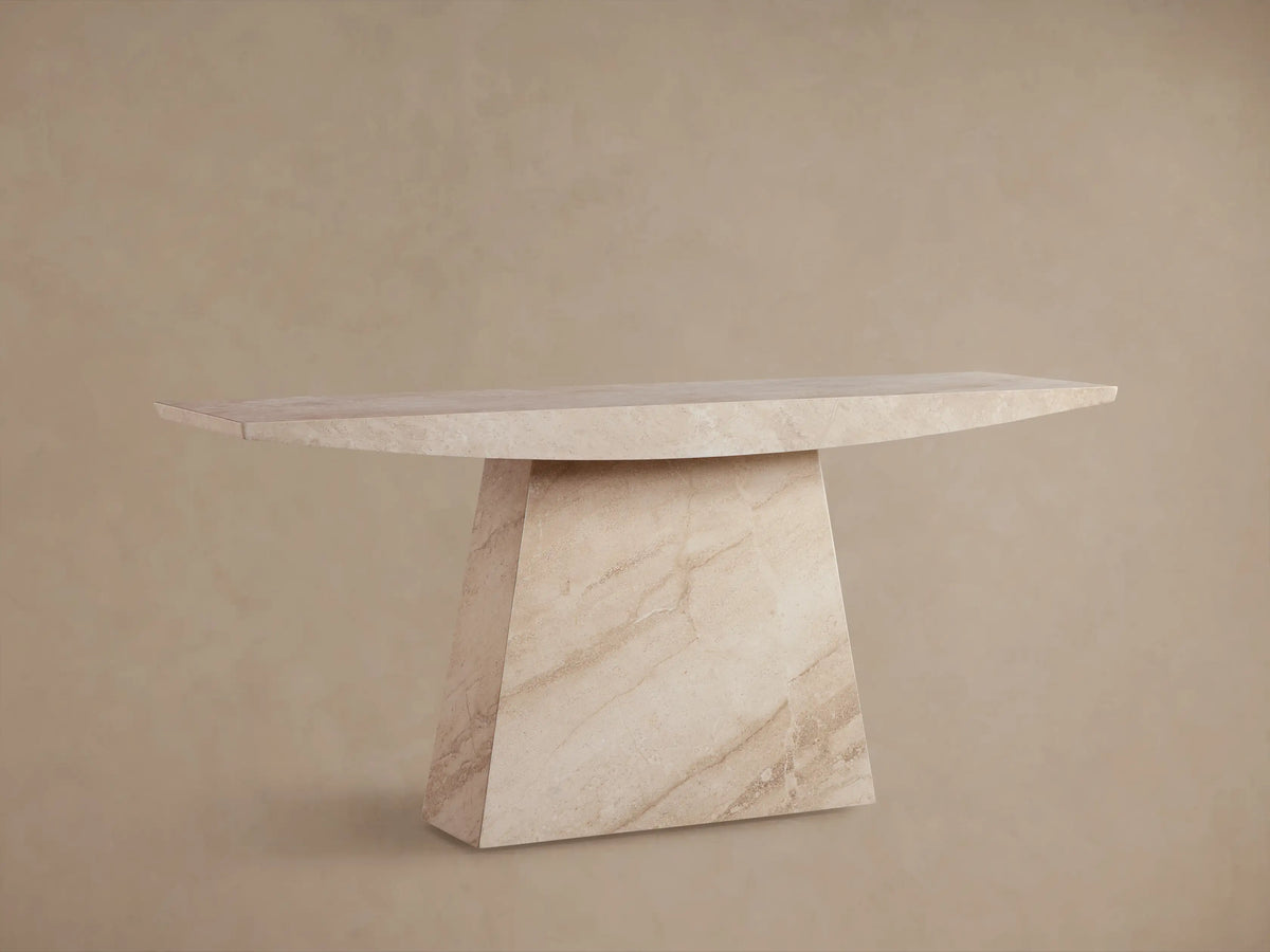 A beige marble console table with a triangular base and a sleek rectangular top, set against a neutral wall and wooden floor.