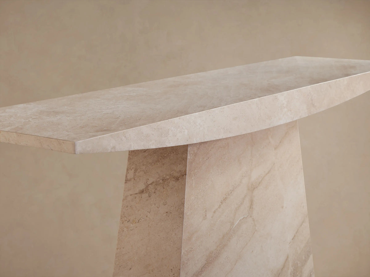 A beige marble console table with an elongated, curved rectangular top and a wide, trapezoidal base on a neutral background.