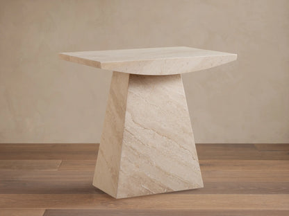 A beige marble side table with a trapezoidal base and a rectangular top, set on a wooden floor against a light wall.