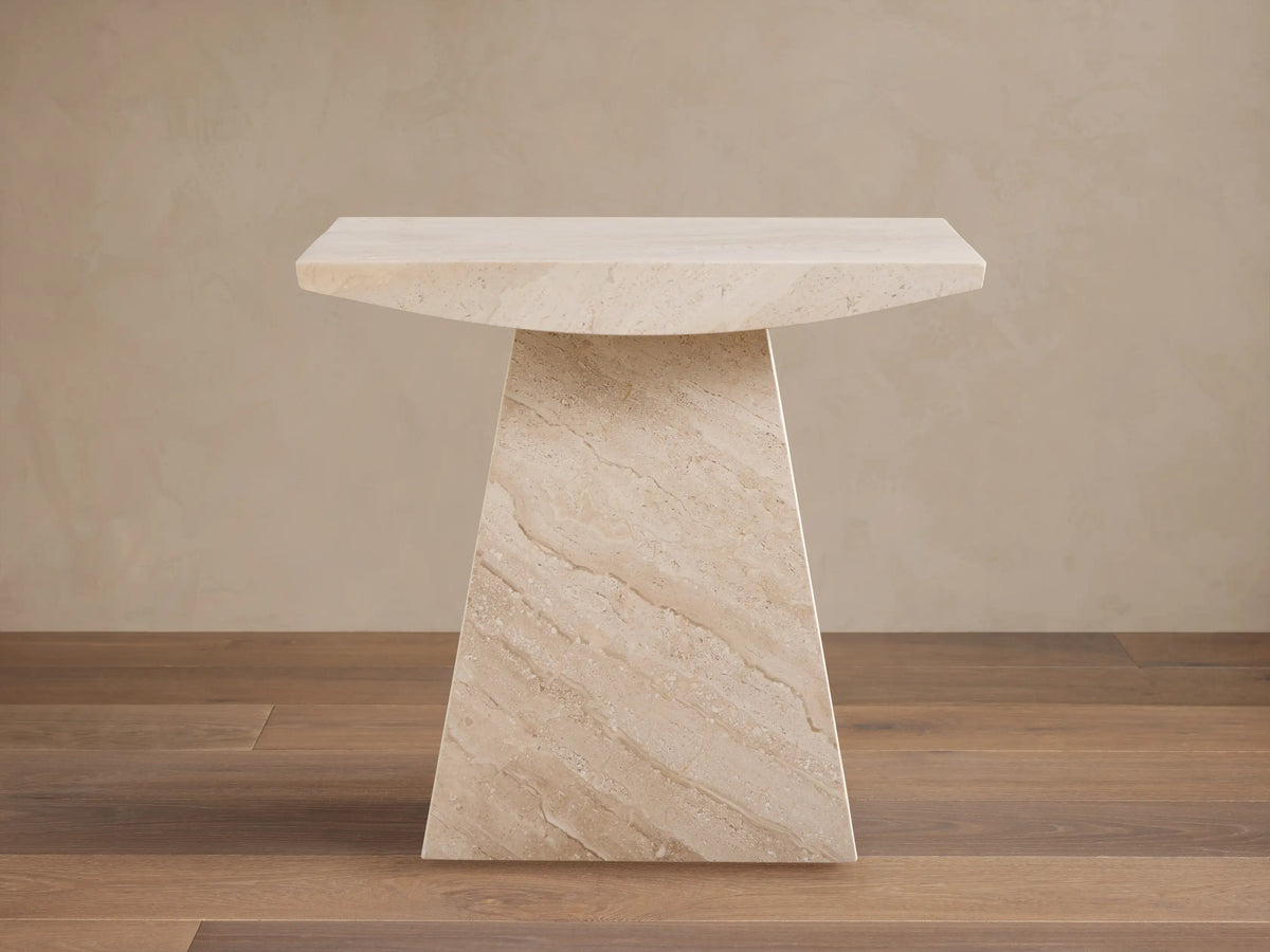 A beige marble side table with a trapezoidal base and a rectangular top, set on a wooden floor against a light wall.